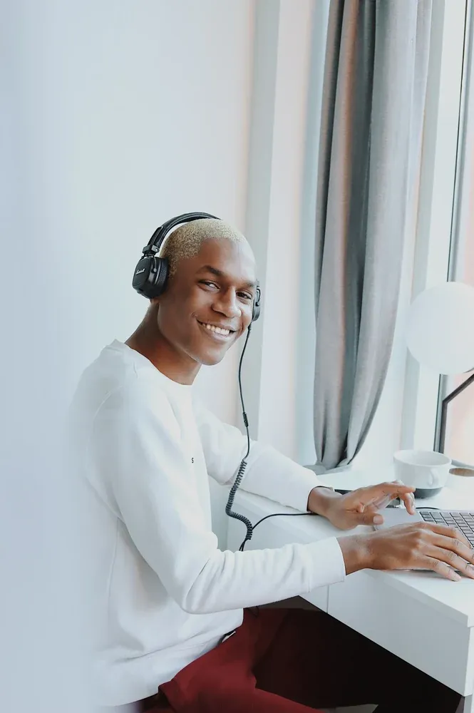 A smiling man with headphones working at his laptop